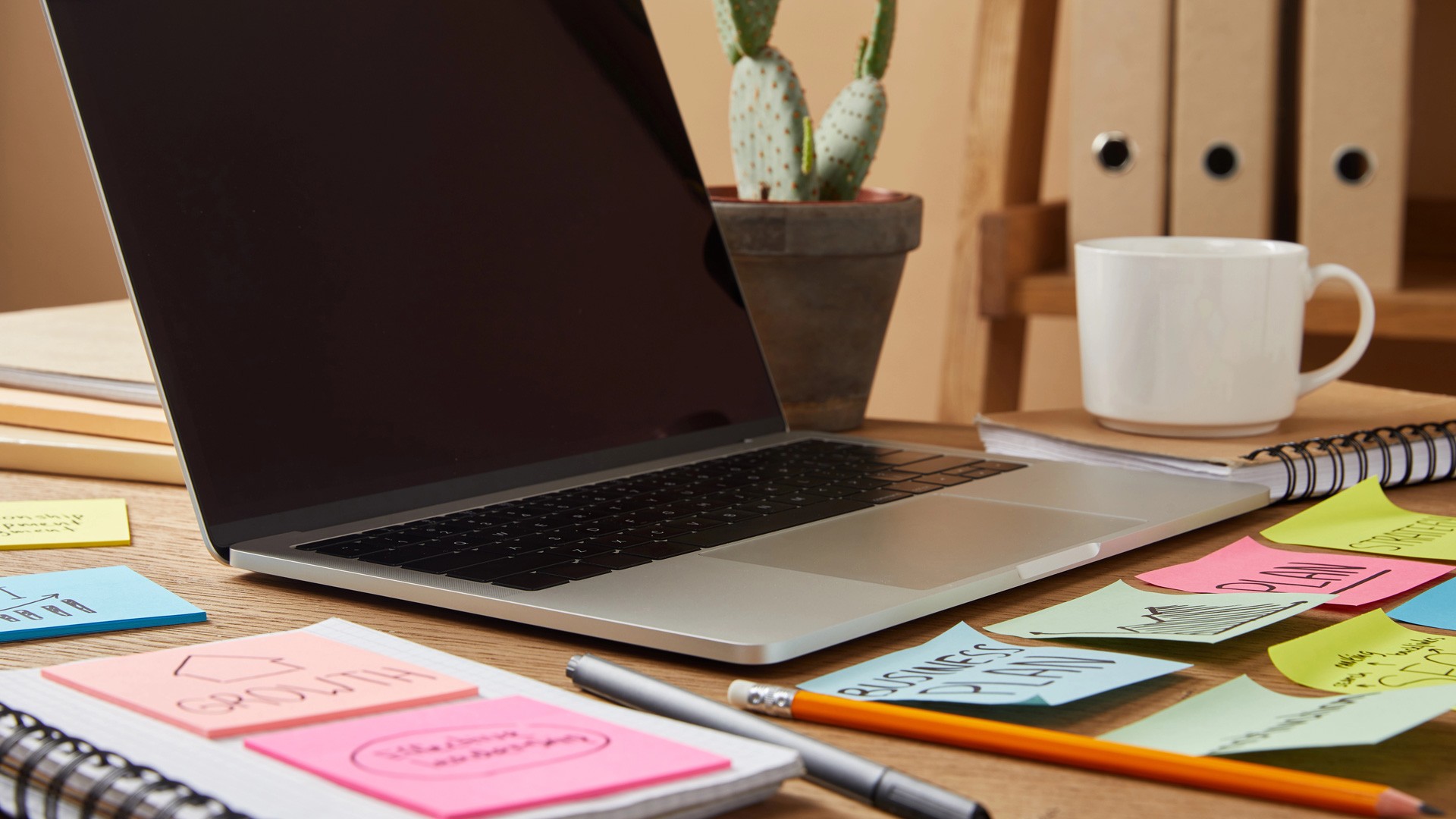 Laptop on organized desk with colorful sticky notes, coffee cup, and notebook – ADHD-friendly business planning workspace
